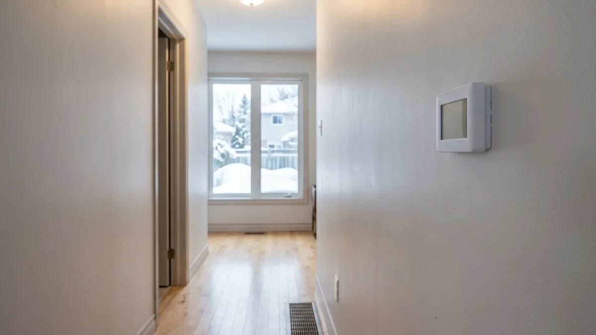 Wall thermostat and floor heat register in a hallway of a Canadian home in winter